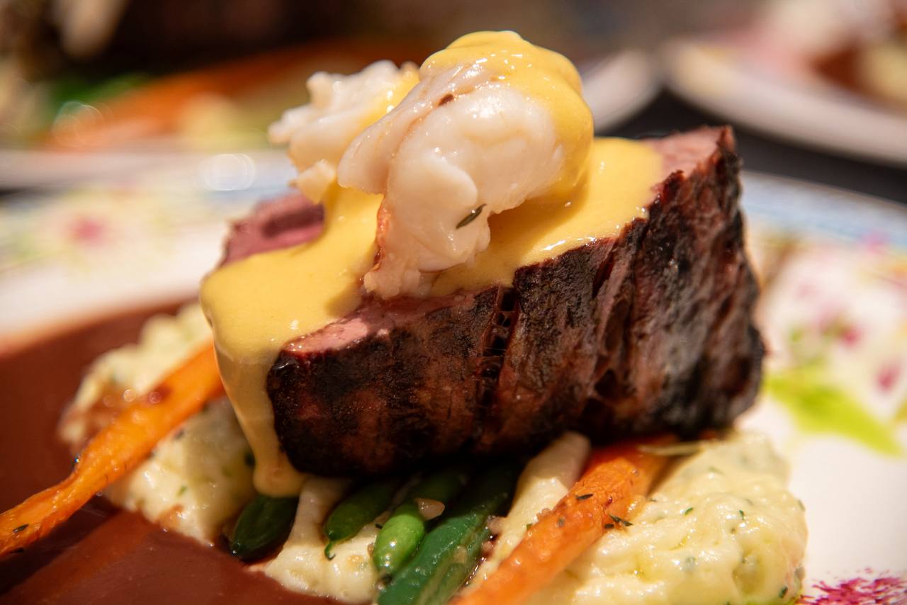 Plated steak topped with seafood and sauce
